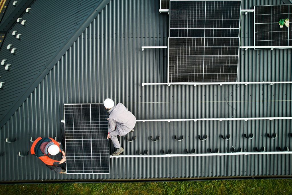 Men workers installing solar panels on roof of house.